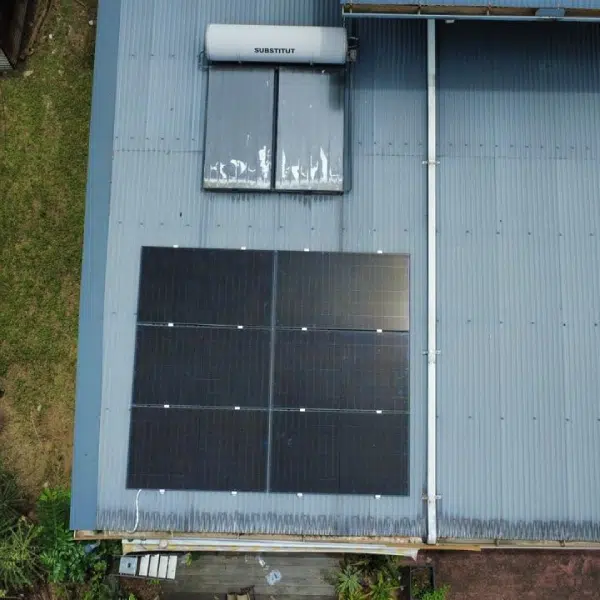 Vue aérienne de deux champs de panneaux solaires et chauffe-eau sur toiture tôle grise en Guyane