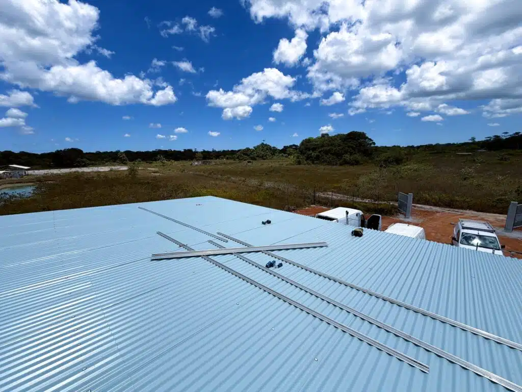 Chantier de site isolé en Guyane : rails de fixation posés sur une grande toiture en tôle, en pleine savane, avant la pose des panneaux solaires