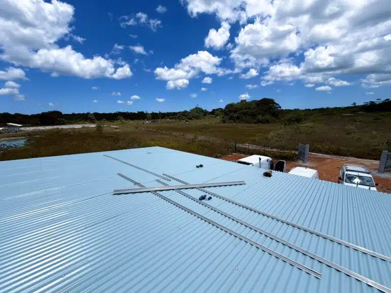 Chantier de site isolé en Guyane : rails de fixation posés sur une grande toiture en tôle, en pleine savane